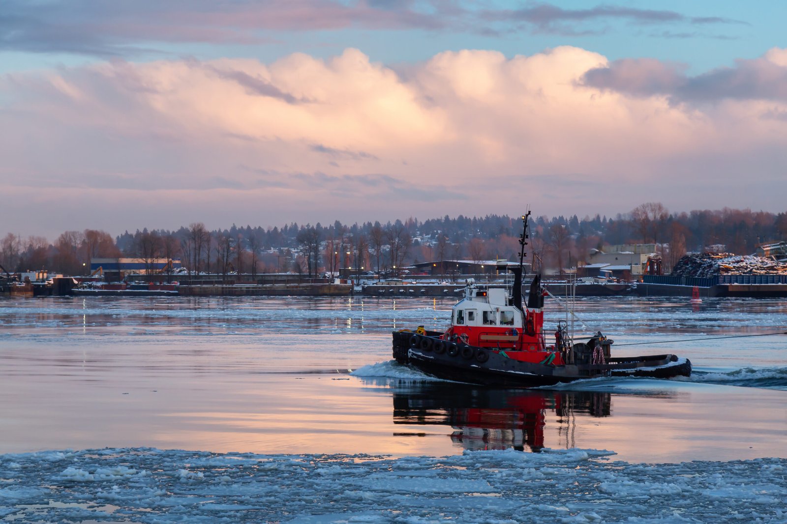 Industrial Tugboat pulling a load in Fraser River during a colorful winter sunset with ice in the water. Taken in New Westminster, Vancouver, BC, Canada.